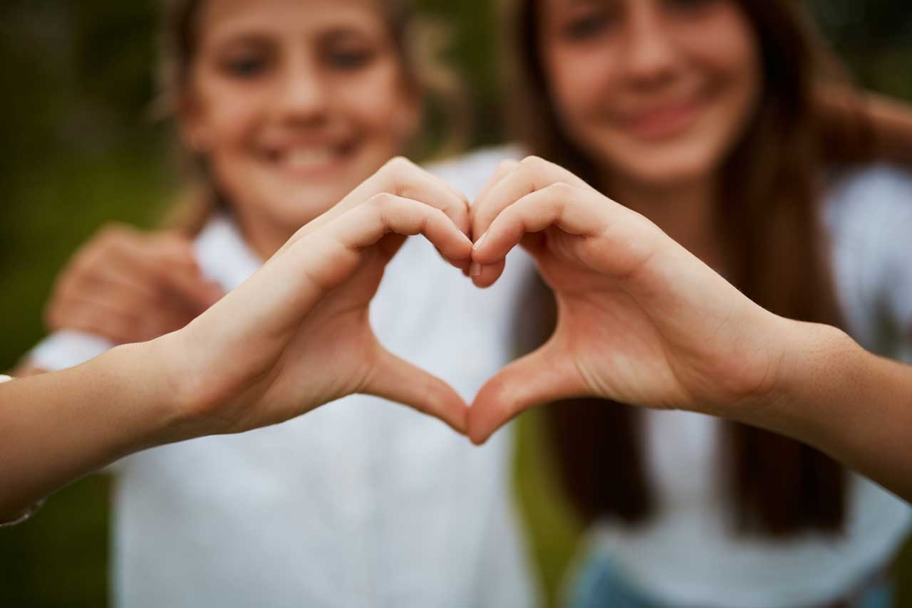 love-hand-sign-happy-sisters-garden-with-fun-relationship-bonding-care-with-siblings-heart-hands-girls-nature-kindness-friendship-teenagers-park-quality-time-together